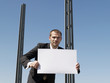 Young man holding sheet of card by concrete pillars