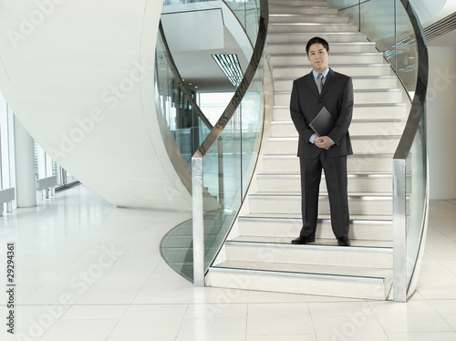 Photo: Confident Businessman, holding folder, standing on stairs Confident Businessman, holding folder, standing on stairs