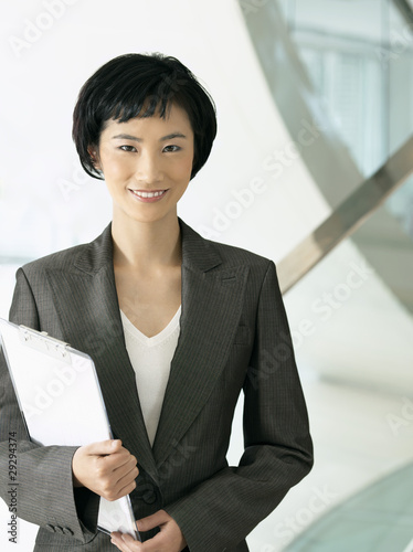 Photo: Smiling businesswoman standing, holding clipboard Smiling businesswoman standing, holding clipboard