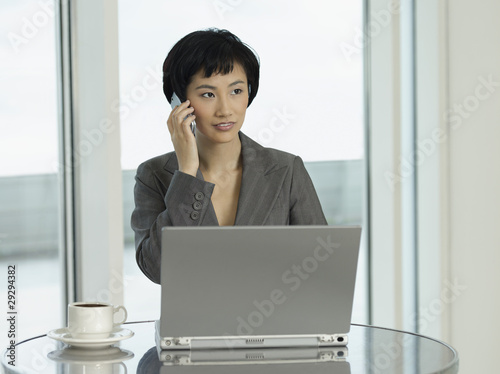 Photo: Businesswoman sitting at table with laptop, talking on phone Businesswoman sitting at table with laptop, talking on phone