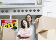 Man and woman with cardboard boxes standing in front of house with sold sign