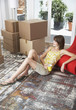 Woman sitting on hardwood floor with mug and cardboard boxes smiling