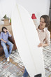 Man with surf board in home with boxes and woman on sofa