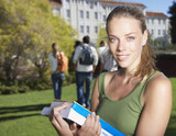 Photo: Young female student standing outdoors with a group of young people in the background Young female student standing outdoors with a group of young people in the background