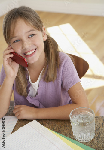Photo: Young girl with mobile phone and homework at kitchen table Young girl with mobile phone and homework at kitchen table