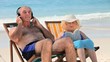 Man listening to music sitting on beach chairs with his wife