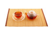 Glass cup of tea and teapot on bamboo placemate isolated