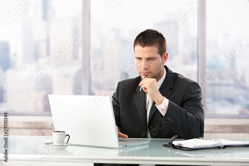 Photo: Young manager working on laptop in office Young manager working on laptop in office