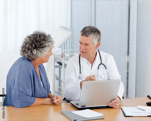 Photo: A senior doctor with his patient looking at the laptop A senior doctor with his patient looking at the laptop