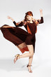 Foto: dancing woman with flying hair and brown elegant dress on gray dancing woman with flying hair and brown elegant dress on gray