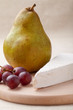 Green pear, cheese brie, red grapes on wooden board macro