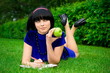 Young beautiful woman lays on green field with apple and book