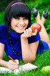 Young beautiful woman lays on green field with apple and book