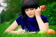 Young beautiful woman lays on green field with apple and book