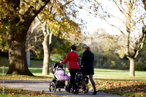 Photo: Two mothers pushing their buggies in the park, rear view Two mothers pushing their buggies in the park, rear view