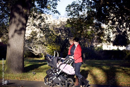 Photo: Two mothers pushing their buggies in the park, smiling Two mothers pushing their buggies in the park, smiling