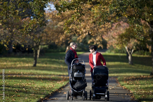 Photo: Two mothers pushing their buggies in the park, laughing Two mothers pushing their buggies in the park, laughing