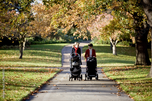 Photo: Two mothers pushing their buggies in the park, talking Two mothers pushing their buggies in the park, talking