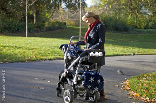 Photo: A mother looking at her babies in a buggy in the park A mother looking at her babies in a buggy in the park