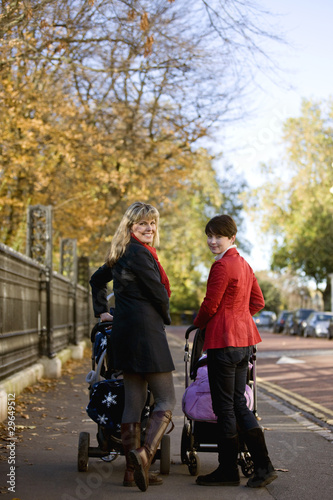 Photo: Two mothers standing with buggies in the street, smiling Two mothers standing with buggies in the street, smiling