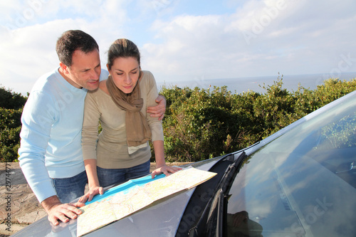Photo: Couple looking at road map on car hood Couple looking at road map on car hood