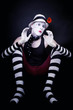 Theatrical mime with red flower sits on the floor