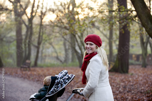Photo: A young mother pushing a stroller in the park A young mother pushing a stroller in the park