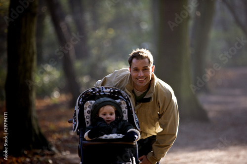 Photo: A young father standing with his son in a stroller in the park A young father standing with his son in a stroller in the park