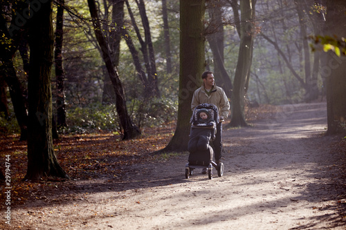 Photo: A young father pushing a stroller in the park A young father pushing a stroller in the park