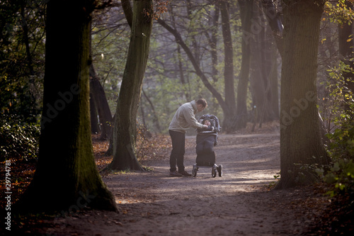 Photo: A young father checking his baby boy in a stroller, in the park A young father checking his baby boy in a stroller, in the park