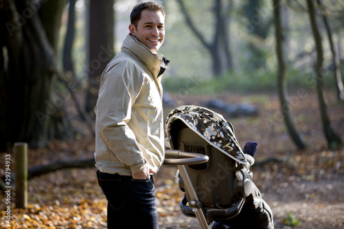 Photo: A young father pushing a stroller in the park A young father pushing a stroller in the park