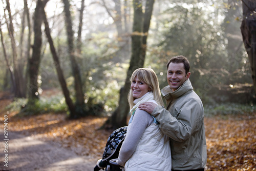 Photo: A young couple pushing a stroller in the park, smiling A young couple pushing a stroller in the park, smiling