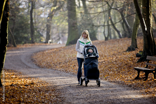 Photo: A young mother pushing a stroller in the park A young mother pushing a stroller in the park