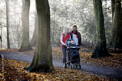 Photo: A young couple pushing a stroller in the park, smiling A young couple pushing a stroller in the park, smiling