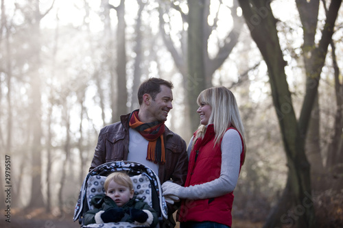 Photo: A young couple pushing a stroller in the park, smiling A young couple pushing a stroller in the park, smiling