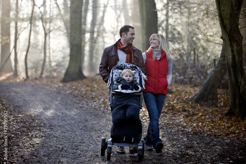 Photo: A young couple pushing a stroller in the park, smiling A young couple pushing a stroller in the park, smiling