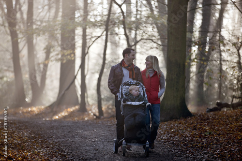 Photo: A young couple pushing a stroller in the park, laughing A young couple pushing a stroller in the park, laughing
