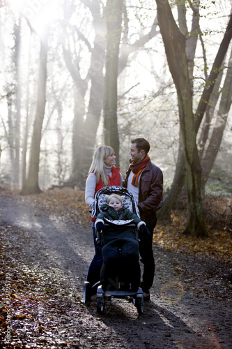 Foto: A young couple standing with a stroller in the park, talking A young couple standing with a stroller in the park, talking