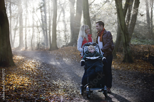 Photo: A young couple pushing a stroller in the park A young couple pushing a stroller in the park