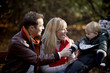 A young couple on a bench, smiling at their son in a stroller