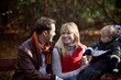 A young couple on a bench, next to their son in a stroller