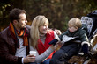 A young couple on a bench, smiling at their son in a stroller