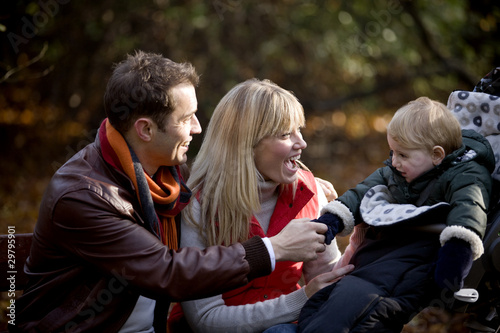 Photo: A young couple on a bench, smiling at their son in a stroller A young couple on a bench, smiling at their son in a stroller
