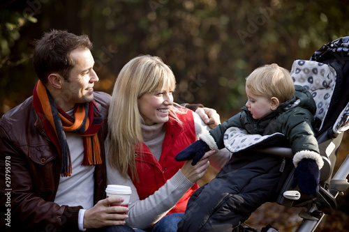 Photo: A young couple on a bench, smiling at their son in a stroller A young couple on a bench, smiling at their son in a stroller