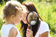 The little girl looks through magnifying glass, which her mother