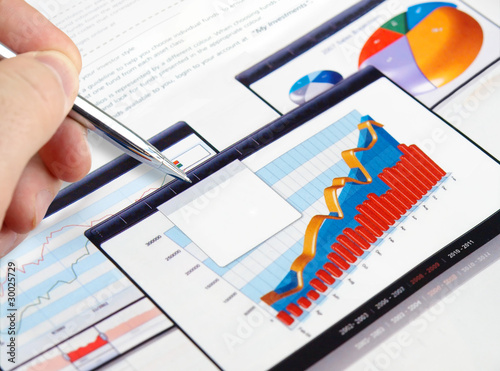 Photo: Male hand with pen on the investment charts Male hand with pen on the investment charts