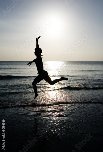 Photo: Woman leaping on the beach at sunset Woman leaping on the beach at sunset