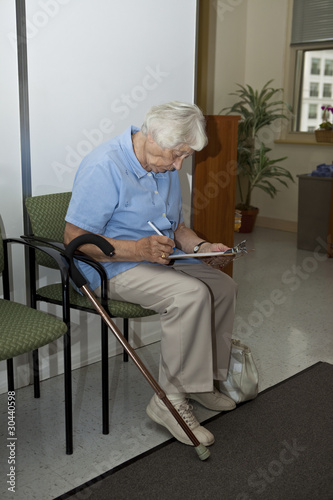 Photo: Senior woman filling out forms at the doctor`s office Senior woman filling out forms at the doctor`s office