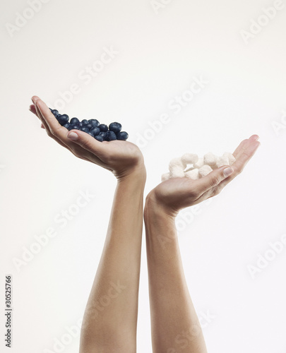 Photo: Woman holding handful of blueberries over handful of sugar cubes Woman holding handful of blueberries over handful of sugar cubes