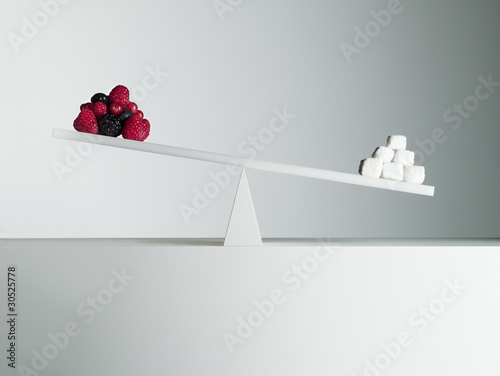 Photo: Sugar cubes tipping seesaw with berries on opposite end Sugar cubes tipping seesaw with berries on opposite end